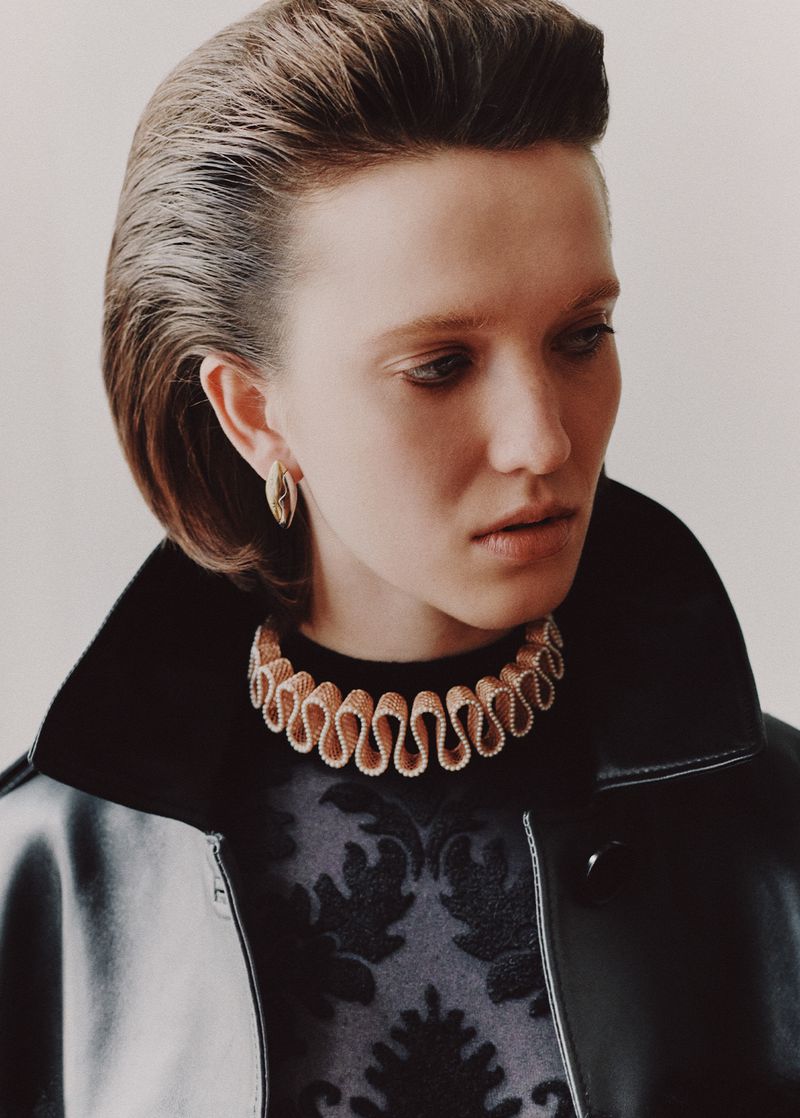 Close-up of a stylish adult female model with glossy dark blonde hair, wearing a black leather jacket and decorative ruffled collar.