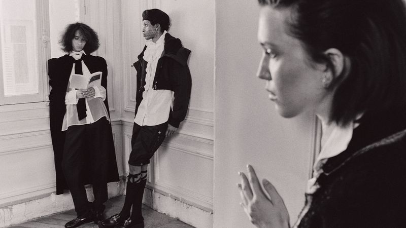 Monochrome fashion shot of three young adults indoors, posing near a window and white wall, wearing vintage-inspired black and white clothing.