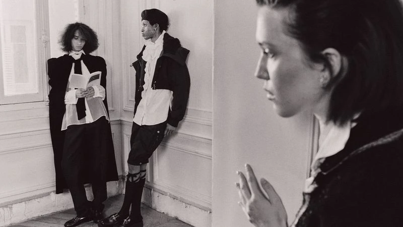 Monochrome fashion shot of three young adults indoors, posing near a window and white wall, wearing vintage-inspired black and white clothing.