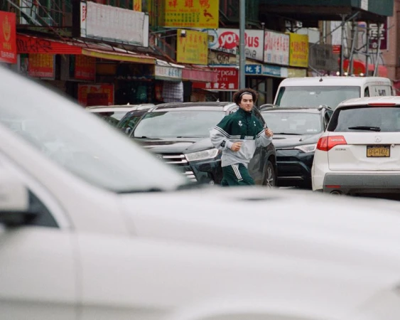 Man in tracksuit jogs in a busy urban street with storefronts and traffic, showcasing an active lifestyle in a city setting.