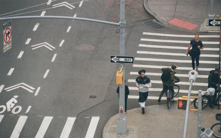 Overhead shot of people crossing a city street in New York with bike lanes, crosswalks, traffic signals, and directional signage.