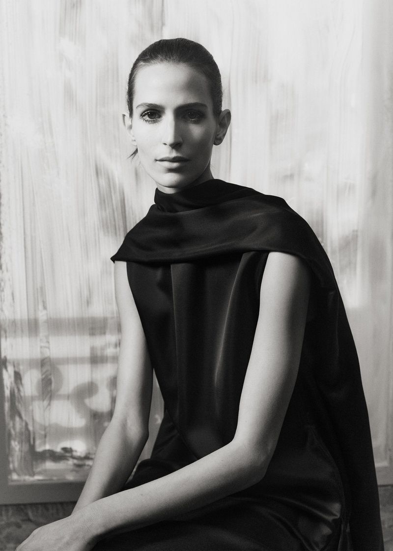 Elegant portrait of a woman in black, seated against a muted backdrop, highlighting fashion and classic style in black and white.