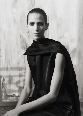 Elegant portrait of a woman in black, seated against a muted backdrop, highlighting fashion and classic style in black and white.