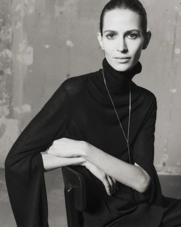 Elegant portrait of a seated adult woman with dark hair wearing a black turtleneck, captured in a monochrome, minimalist setting.