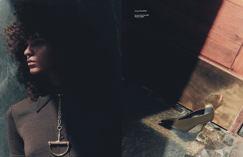 Indoor fashion shot with a woman wearing a brown top and silver necklace and a silver heel on a marble floor, shadowed lighting.