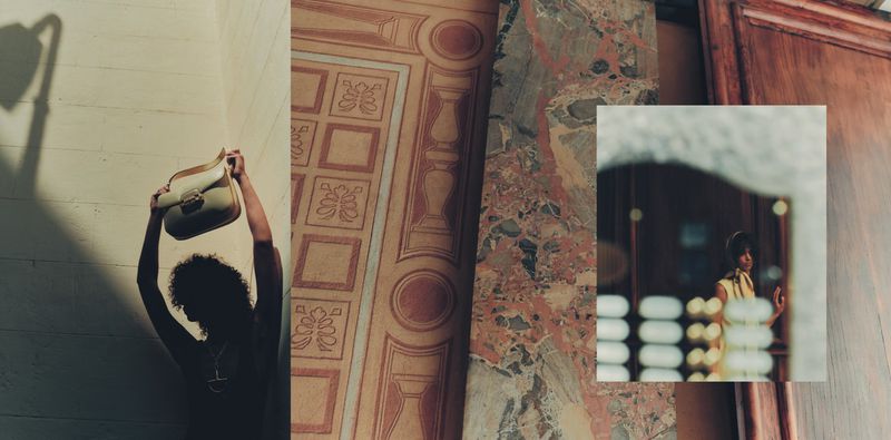 Woman holds a cream-colored handbag against a white wall with shadow. Architectural details of marble and doorway in the background.