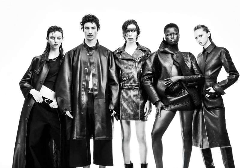 Five fashion models in black leather outerwear stand in a studio setting against a white backdrop, showcasing a contemporary, high-fashion aesthetic.