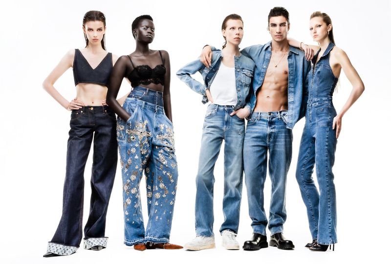 Five fashion models in denim outfits pose against a white backdrop showcasing various washes, styles, and embellishments of jeanswear.