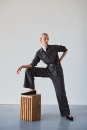 Model Jean Campbell posing with one foot on a wooden block wearing a dark jumpsuit for ME+EM