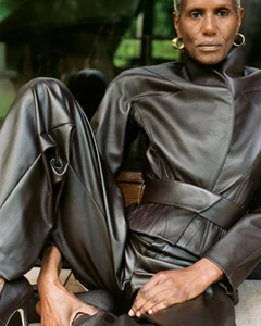 Model Amanda Parker seated in a dark brown leather high-neck jacket and matching wide-leg trousers outdoors.