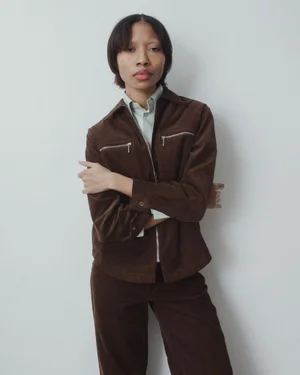 Model Dominique Babineaux wearing a brown corduroy zip-up jacket and trousers against a pale studio wall.