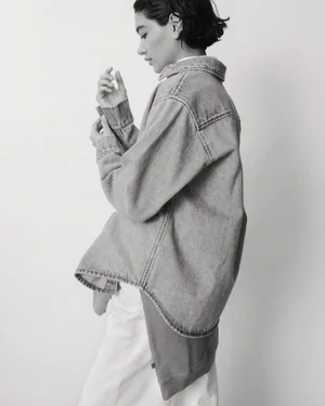 Model in denim shirt and light trousers posing against a white background for Still Here lookbook