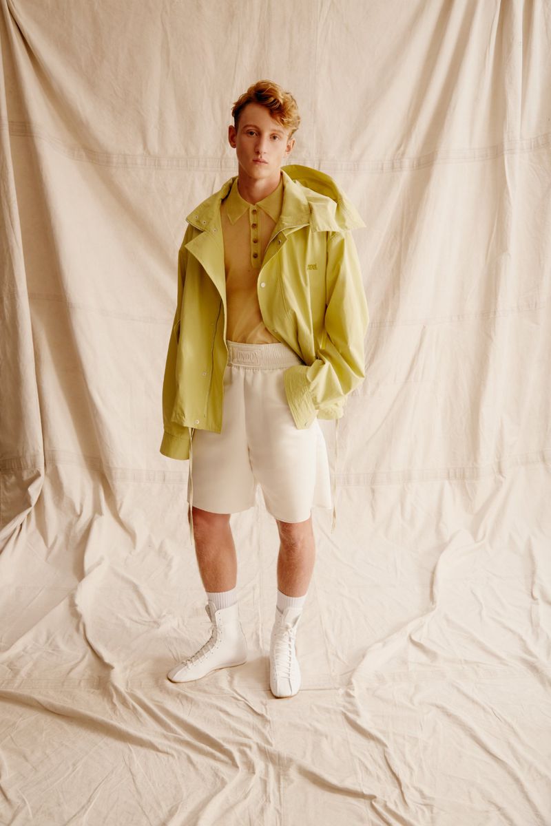 Male model in lime jacket and shorts poses in a studio against a cream-colored backdrop, showcasing modern casual fashion.