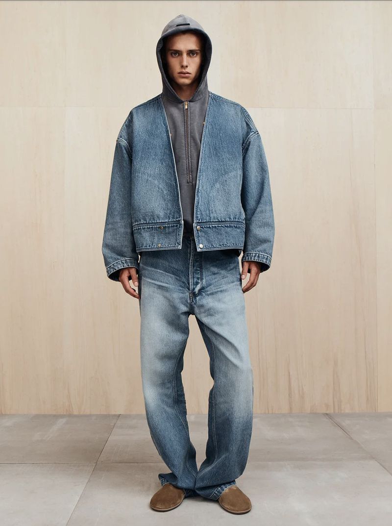 Adult male wearing a denim jacket and jeans stands against a neutral backdrop in a fashion shot emphasizing the textures and color palette.