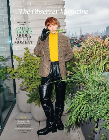 Fashion magazine cover featuring a red-haired man in stylish jacket and leather trousers, holding a pea pod in his mouth, with a city backdrop.