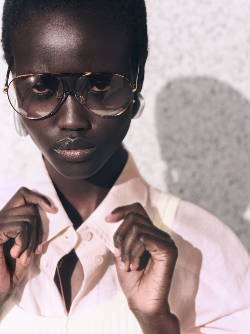 Close-up portrait of a black woman wearing aviator sunglasses and a light-coloured collared shirt for COS