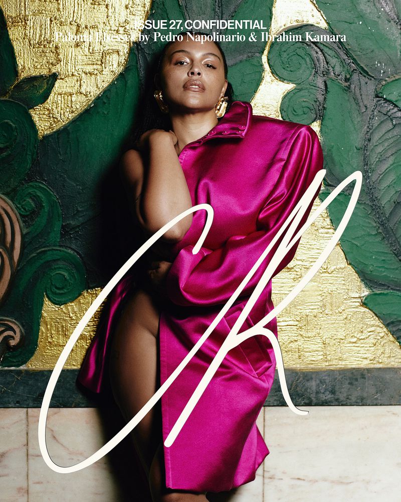 Fashion magazine cover featuring a woman in a magenta satin dress, artistic gold and green backdrop, and stylized white text overlay.