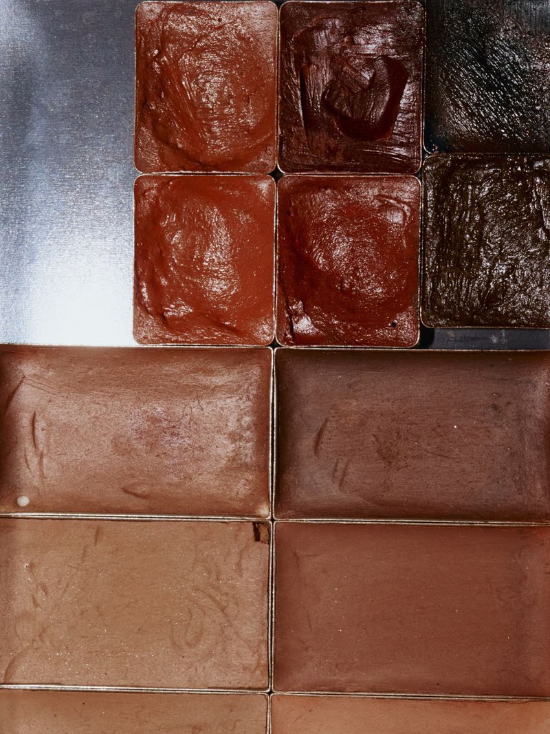 Makeup palette featuring rows of square containers with different shades of brown and bronze foundation, concealer, or cream eyeshadow.