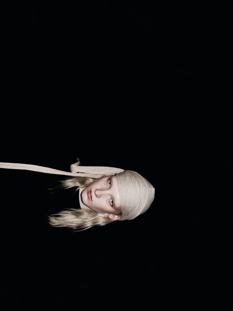 Woman with blond hair and a white bandage on her head poses against a black background in a dramatic and artistic beauty shot.