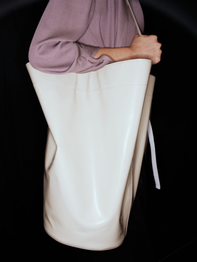 Person carrying a large, light-colored leather tote bag against a dark background, showcasing fashion accessory and design.