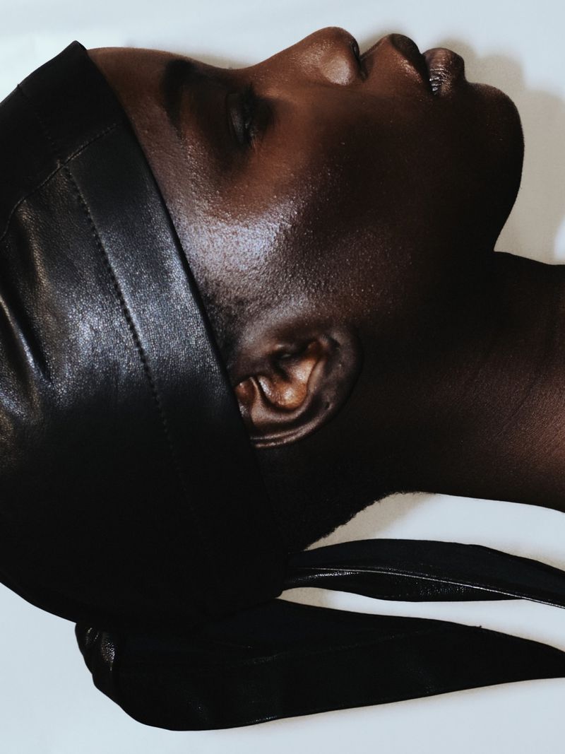 Close-up studio portrait of an adult Black male with a durag, showcasing his face and neck against a light, neutral background.