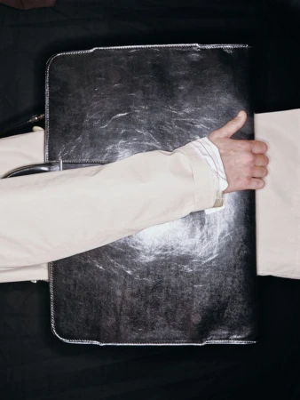 Overhead studio shot of a man's hand holding a closed, shiny black document briefcase against a dark backdrop.