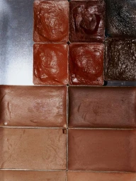 Close-up of a professional cream makeup palette with assorted brown, nude, terracotta, and deep shade pans arranged in metal trays.