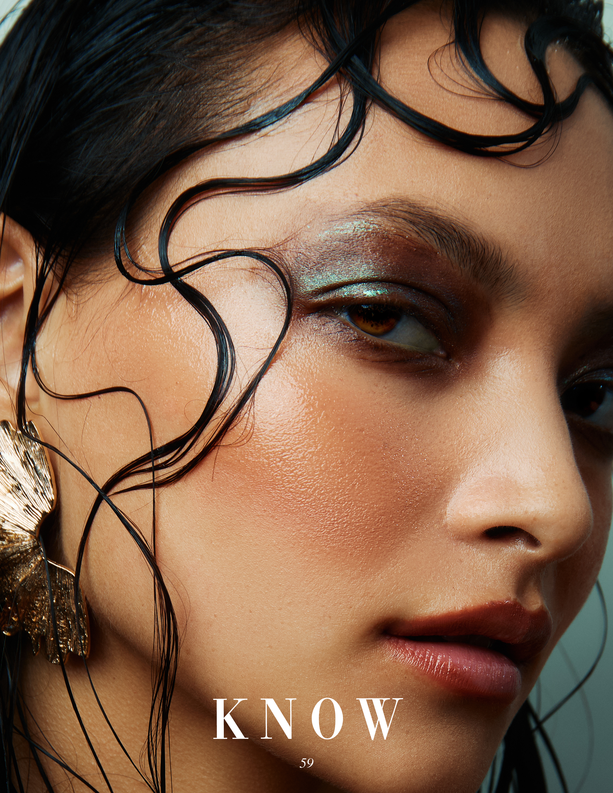 Close-up portrait of a woman with wet hair, striking eyeshadow, and statement earrings in a studio setting, beauty and fashion.