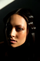 Close-up portrait of a woman with sculpted wave hair and warm makeup illuminated by dramatic diagonal chiaroscuro light.
