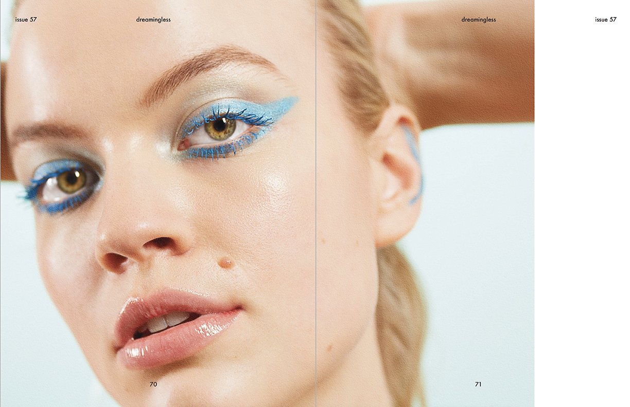 Close-up of a young adult female model with blue eyeshadow and glossy lips on a light blue background in a beauty editorial spread.