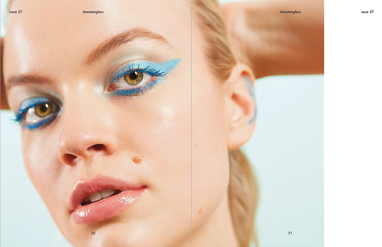 Close-up beauty portrait of a woman with vibrant blue winged eyeliner, blue mascara, and glossy lips for an editorial spread.
