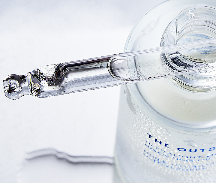 Close-up of clear serum dropper, focus on the product against a bright white backdrop, showcasing skincare and beauty photography.