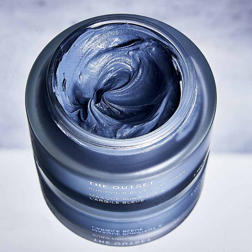 Elevated view of a jar of blue clay mask from The Outset skincare line, offering a glimpse into the product's texture and consistency.