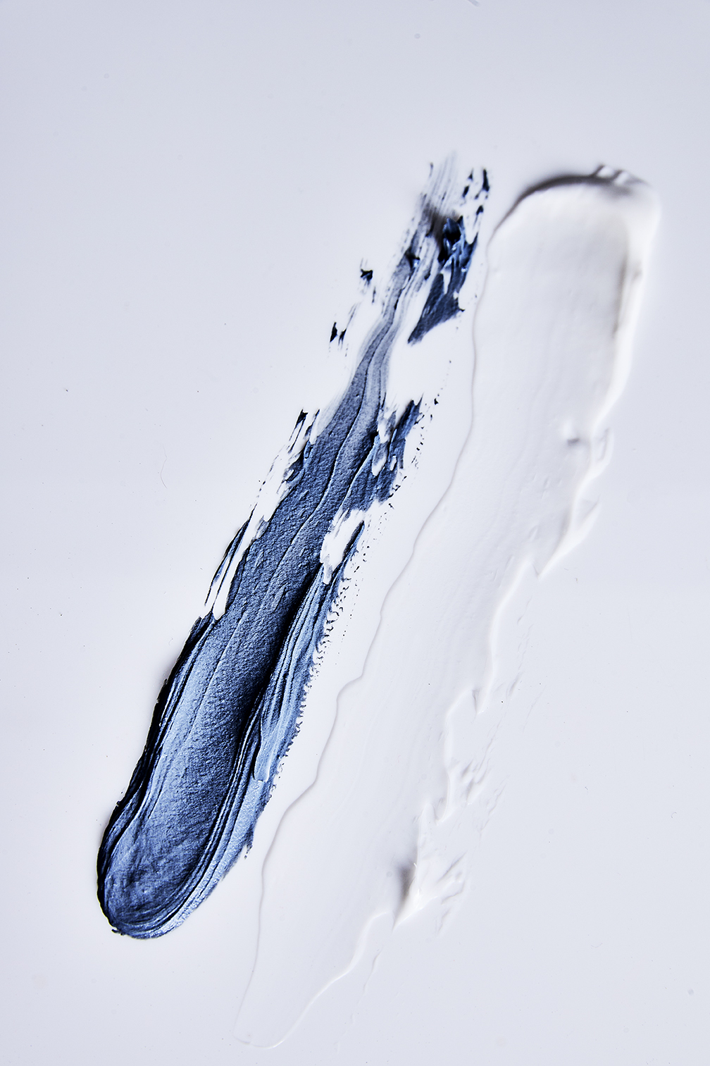 Abstract beauty shot featuring two contrasting cosmetic smears, one in a deep blue and the other in a lighter white, on a white background.
