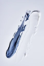 Close-up of blue clay mask and white cream skincare swatches smeared diagonally across a white studio backdrop.