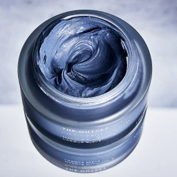An open jar of The Outset Purifying Blue Clay Mask with rich swirling blue cream displayed on a reflective white surface.