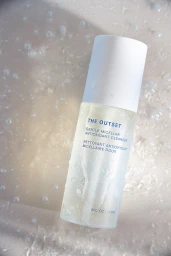 The Outset Gentle Micellar Antioxidant Cleanser bottle resting in clear rippling water with visible droplets on the surface.