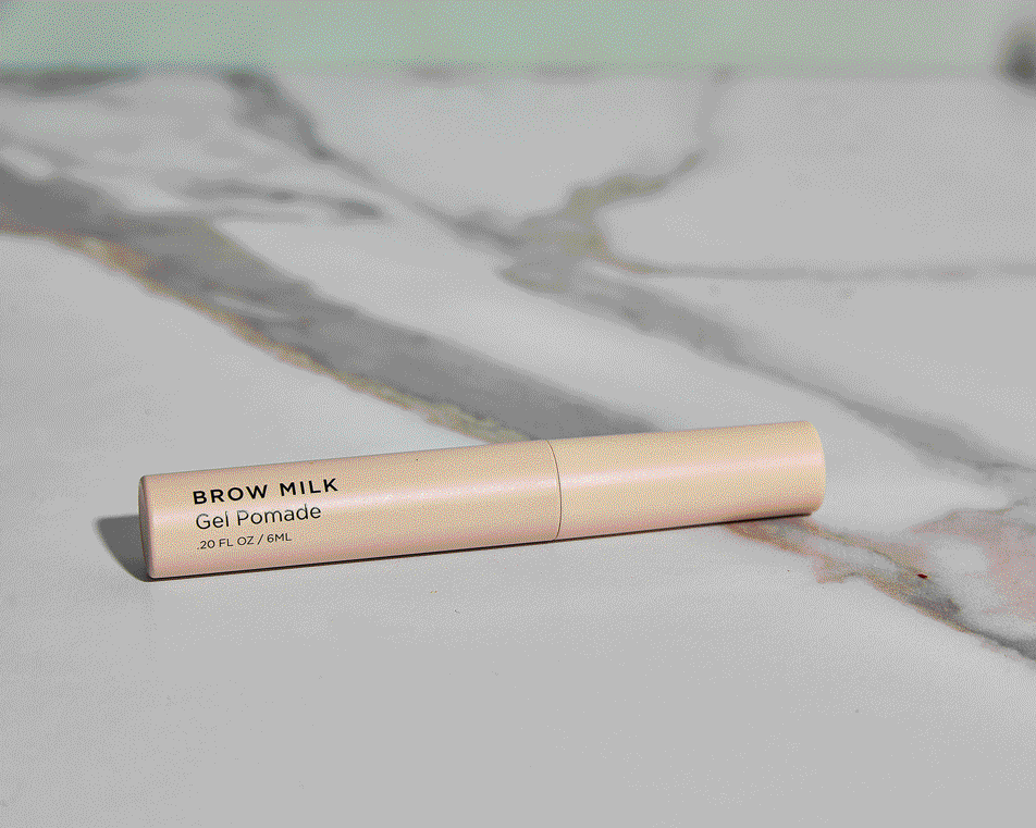 Peach brow gel pomade product on a white marble surface. Minimalist beauty product photography for social media and e-commerce.