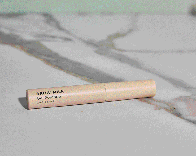 Peach brow gel pomade product on a white marble surface. Minimalist beauty product photography for social media and e-commerce.