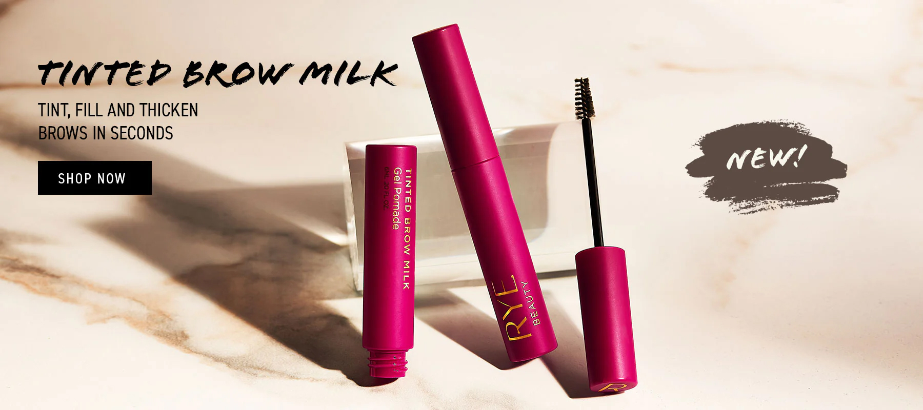 Cosmetic still life featuring magenta-colored brow milk product and applicator brush on a marble surface with soft studio lighting.