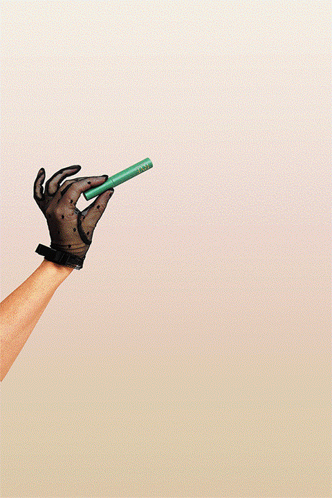 Gloved hand holds a green cosmetic tube against a light background, suggesting beauty and personal care product promotion.