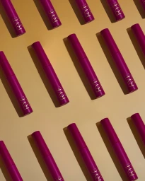 Pattern of magenta Rye Beauty cosmetic tubes arranged diagonally across a warm beige background with directional shadows.