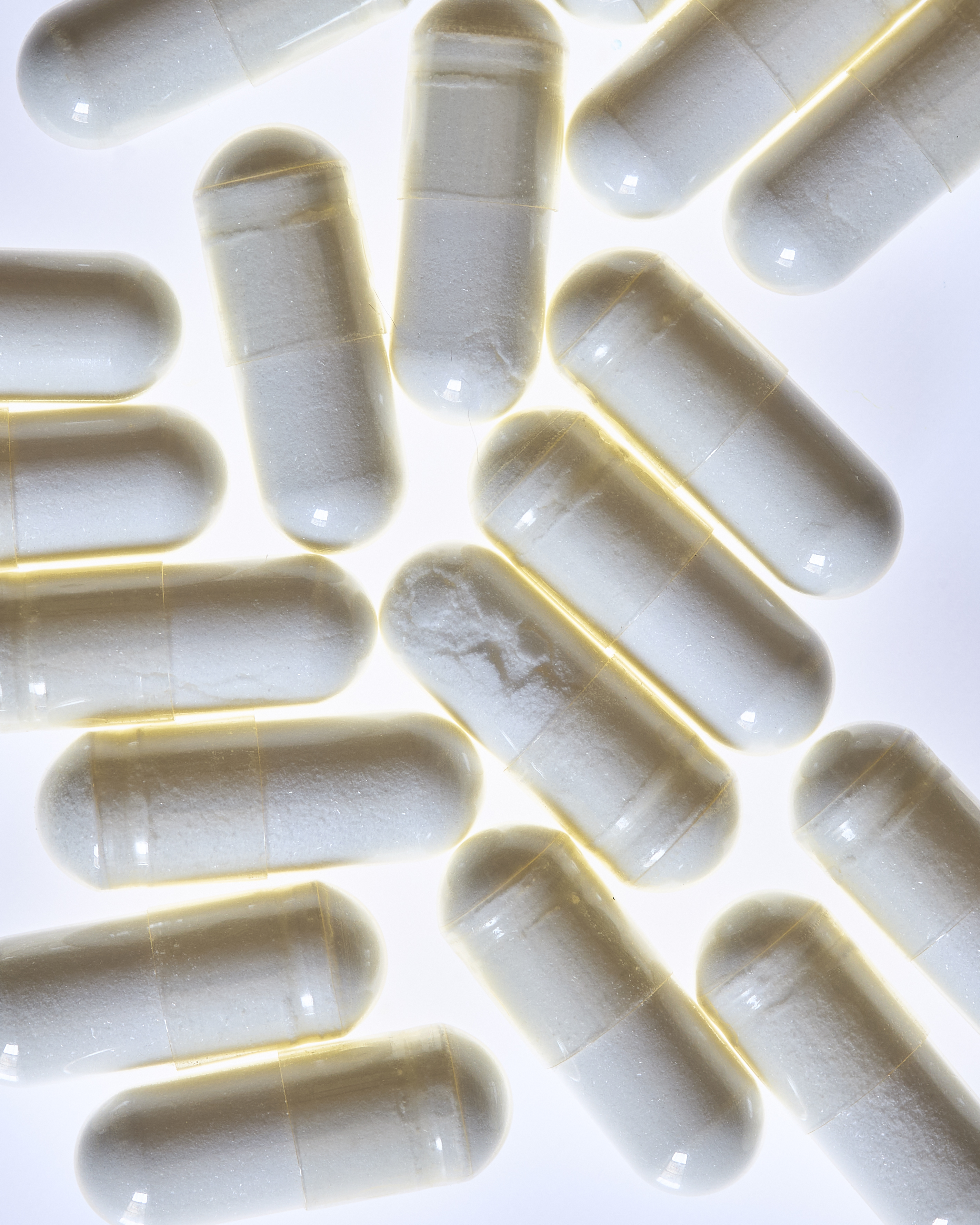 Numerous white capsules arranged closely together, creating a dense and clean pattern. The pills are brightly lit and stand out.