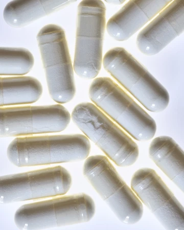 Numerous white capsules arranged closely together, creating a dense and clean pattern. The pills are brightly lit and stand out.