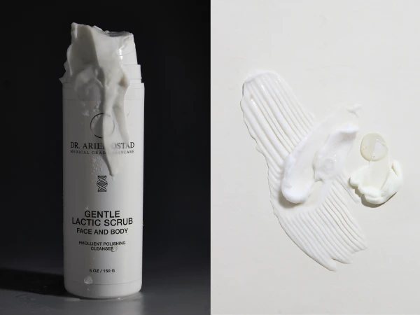 Cosmetic product photography featuring a white bottle of lactic scrub with a smudge of white cream on a split cream and black background.