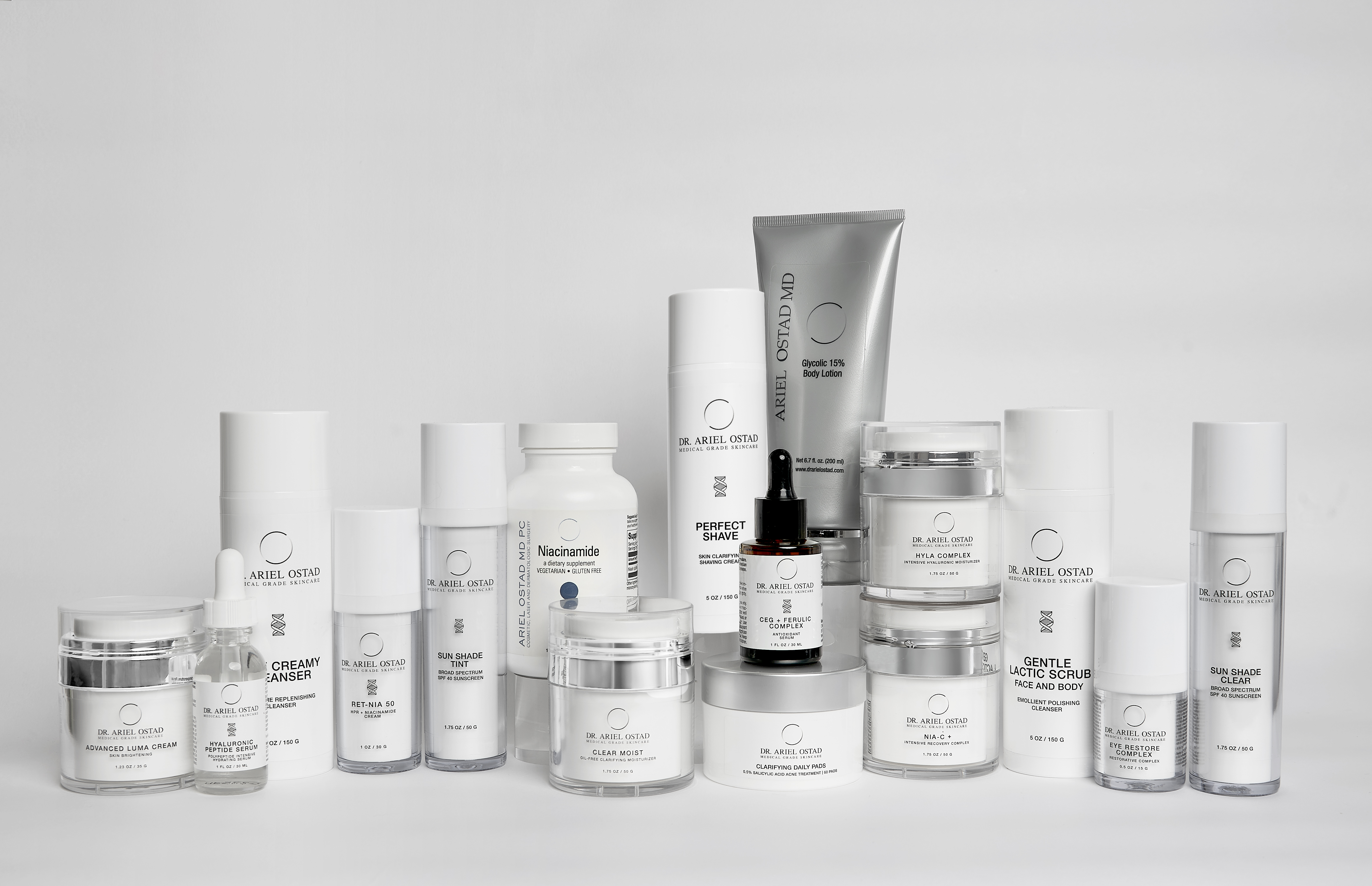Collection of Dr. Ariel Ostad skincare products in white packaging, including cleansers, scrubs, lotions, and serums, displayed on a white surface.