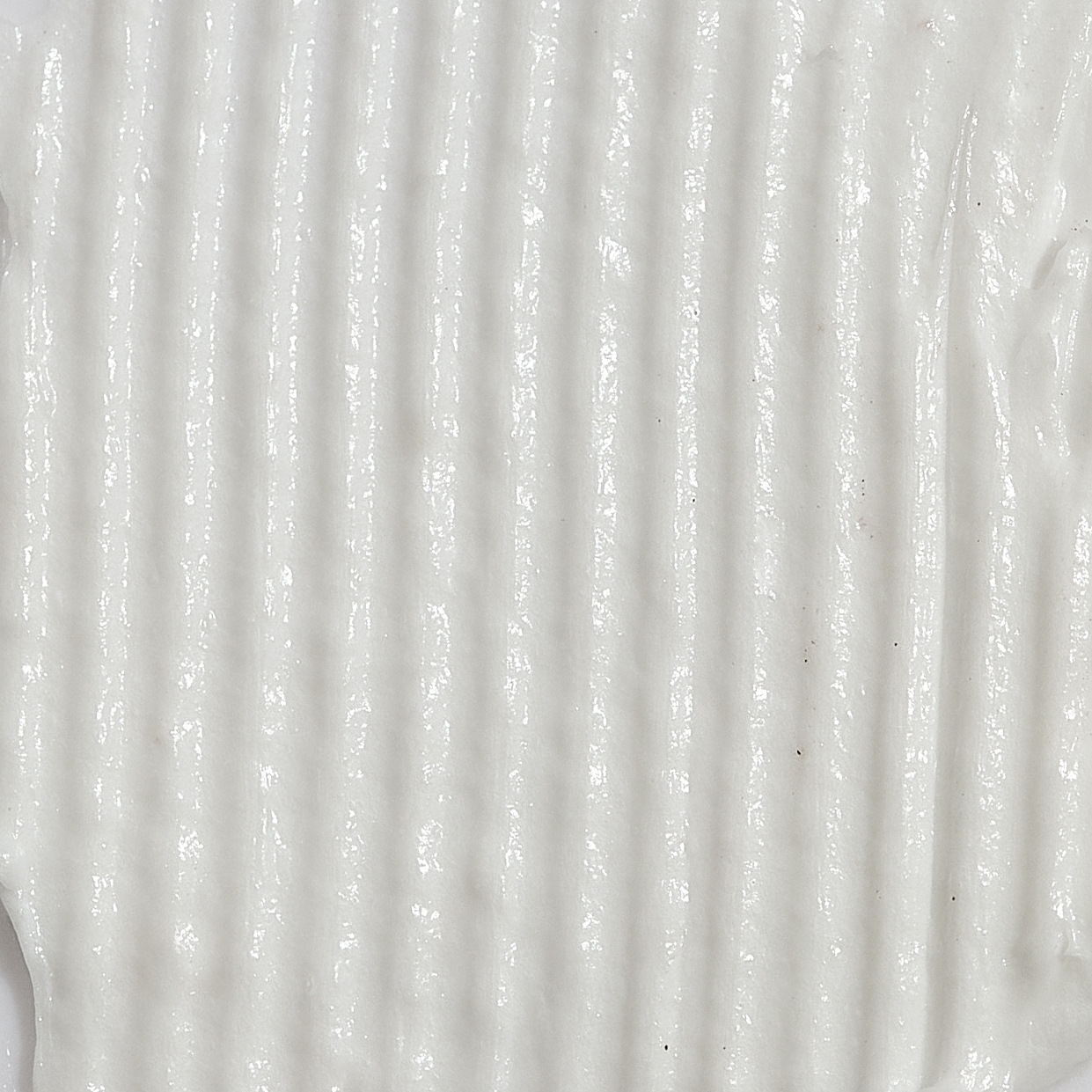 Close-up texture shot of a smooth, white cream with a linear ribbed pattern and a glossy sheen.