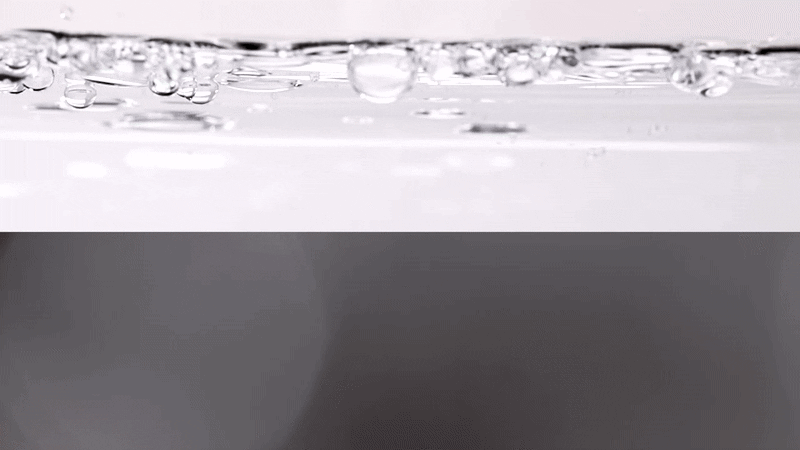 Close-up shot of water with bubbles against a background that transitions from white to dark gray, creating a visually simple and clean composition.