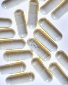 Close-up overhead view of multiple white powder-filled supplement capsules backlit on a bright white surface.