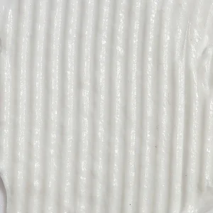 Macro shot of thick white skincare cream spread into combed vertical ridges across the full surface.